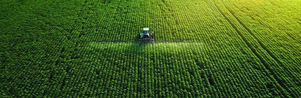 Tracking shot. Drone point of view of a Tractor spraying on a cultivated field. Small Business.